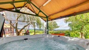 Un jacuzzi bajo un toldo de madera con vistas a un paisaje verde.
