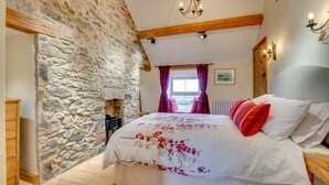Un dormitorio con pared de piedra, una cama con ropa de cama floral, cabecera de madera y una araña.