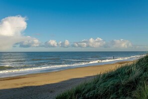 A beach with waves, a clear sky, and some clouds.