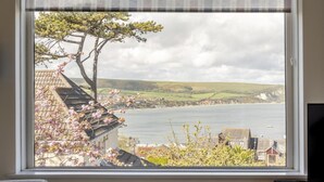 Vista costera desde una ventana con vistas al mar, un árbol y un paisaje lejano.