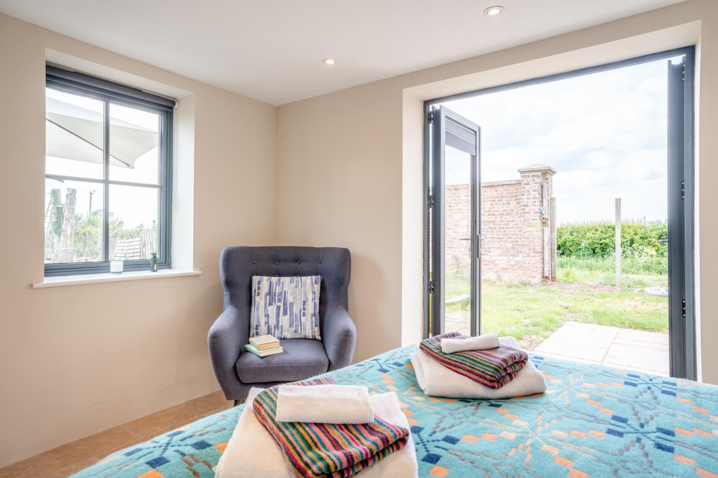 Ein Zimmer mit großem Fenster, einem Sessel mit Kissen und einem Bett mit gemustertem Überwurf.