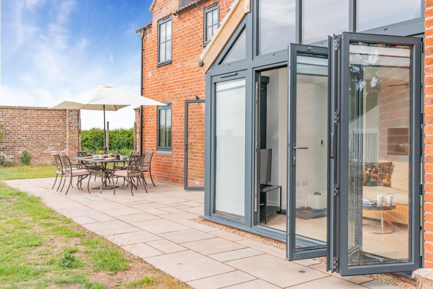 Een modern huis met een terras, een eethoek met tuinmeubilair en een glazen deur die naar een binnenruimte leidt.