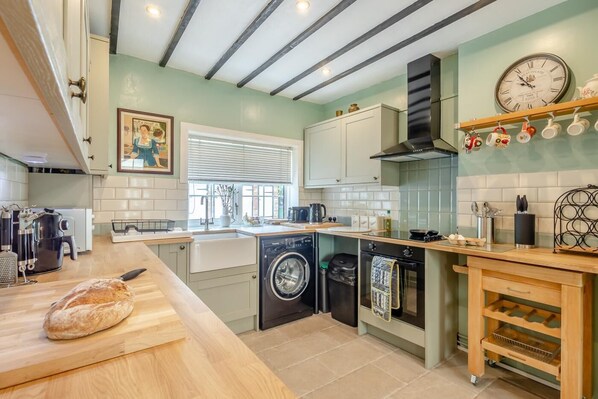 A compact kitchen with a built-in washing machine, a coffee maker, and a wooden countertop. - 3 Bed in Hythe (oc-o31997) (Hythe)
