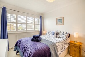 Ein Schlafzimmer mit einem Bett, zwei Nachttischlampen, einem fenster mit Vorhängen, einer Heizung und einem gerahmten Bild an der Wand.