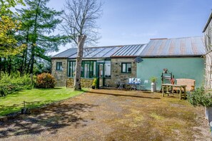 A stone house with a green exterior and a metal roof. There is a patio with outdoor furniture and a garden area with trees and shrubs. - 1 Bed in Catton (oc-b31984) (Catton)