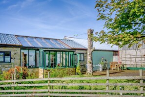 A stone house with a green-framed conservatory, a wooden fence, and a tree in the foreground. - 1 Bed in Catton (oc-b31984) (Catton)