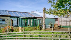 A stone house with a green-framed conservatory, a wooden fence, and a tree in the foreground. - 1 Bed in Catton (oc-b31984) (Catton)