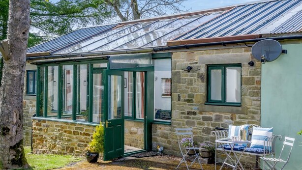 A stone cottage with a green door and windows, a small garden with a bench, and a metal roof. - 1 Bed in Catton (oc-b31984) (Catton)