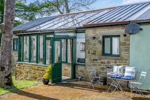 A stone cottage with a green door and windows, a small garden with a bench, and a metal roof. - 1 Bed in Catton (oc-b31984) (Catton)