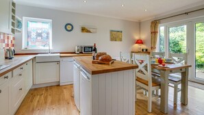 Een compacte keuken met witte kastjes, een houten aanrechtblad, een spoelbak, een magnetron, en een eethoek met een tafel en stoelen.