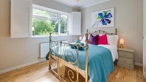Een slaapkamer met een bed, nachtkastje en een raam met luiken.