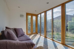 A modern living room with a sofa, large windows, and a view of the outdoors. - 2 Bed in Old Hunstanton (oc-2036) (Hunstanton)