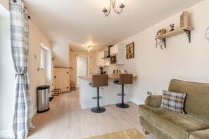 A modern kitchen with a central island, two bar stools, a sofa, and a dining area with a table and chairs. - 2 Bed in Bewdley (oc-n31968) (Bewdley)