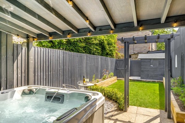 A hot tub under a wooden pergola with a wooden fence and a grassy yard in the background.