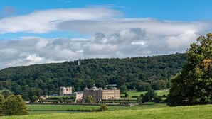 A large historic building with a symmetrical facade, surrounded by lush green fields and a forested hill in the background. - 1 Bed in Darley Dale (oc-w32014) (Northwood and Tinkersley)