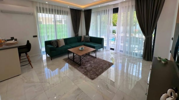 A modern living room with a green sofa, a coffee table, and a dining area with a bar.