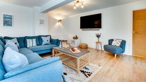 A modern living room with a sectional sofa, a coffee table, and a TV mounted on the wall. - 3 Bed in Padstow (oc-p00793) (Padstow)