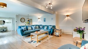 A spacious living room with a blue sofa set, a wooden coffee table, and a dining area with a white table and chairs. - 3 Bed in Padstow (oc-p00793) (Padstow)