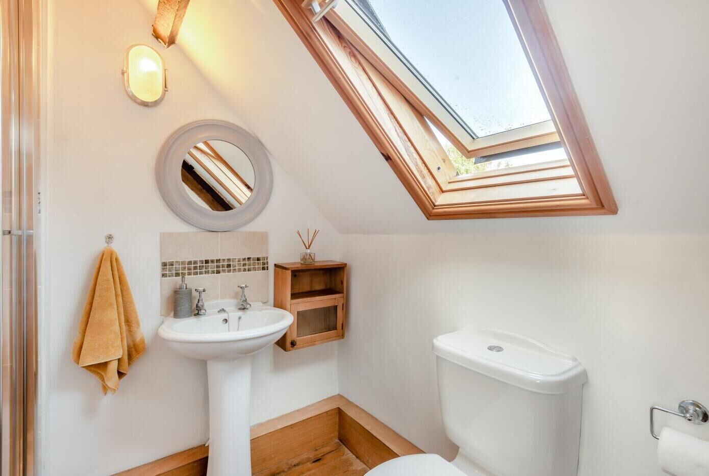 A small, modern bathroom with a skylight, a round mirror, a white sink, and a toilet.