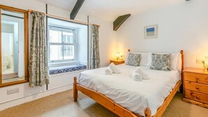 A bedroom with a wooden bed, a window with curtains, a bedside table with a lamp, and a small picture on the wall. - 2 Bed in St. Ives (oc-b31979) (St Ives)