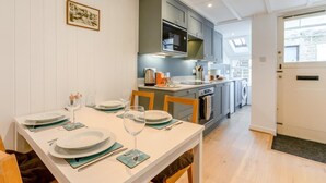 A dining area with a table set for four, a kitchen with modern appliances, and a laundry area visible through an open door. - 2 Bed in St. Ives (oc-b31979) (St Ives)