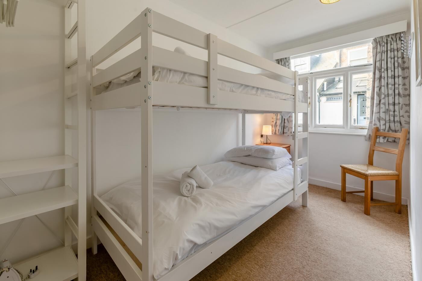 A bunk bed room with a wooden chair and a window with curtains.