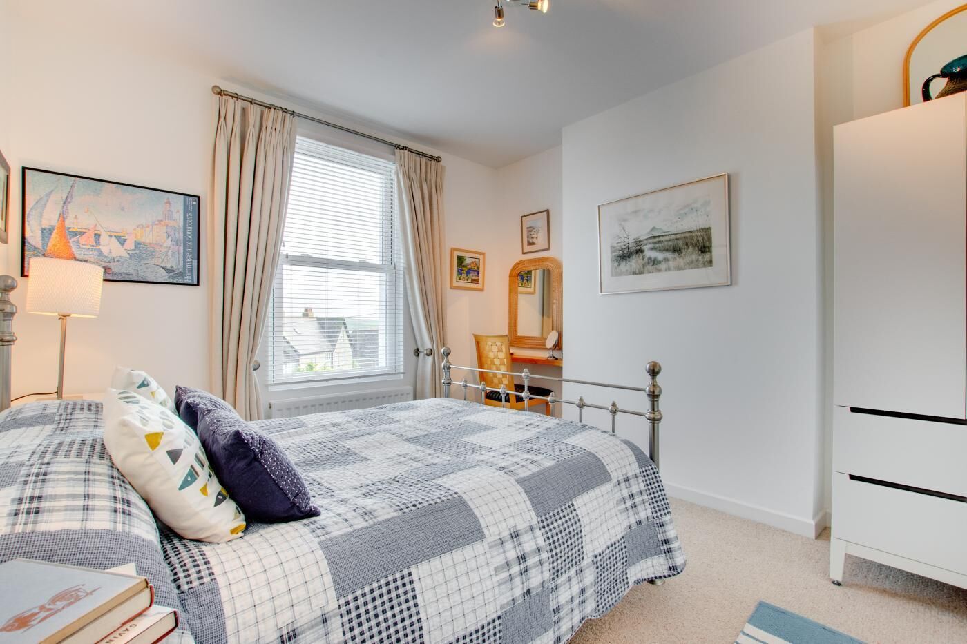 A bedroom with a bed, a nightstand, a dresser, a window with curtains, and wall art.
