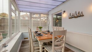 En matplats med ett bord dukat för fyra personer, vita stolar, ett träbord och ett fönster med persienner.