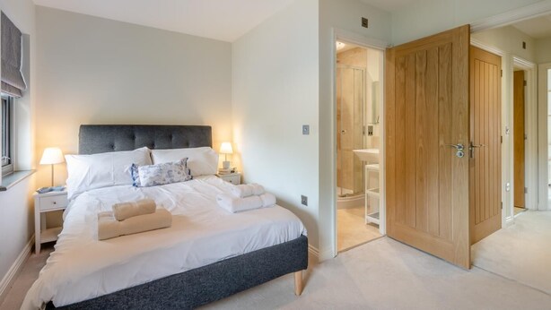 A bedroom with a large bed, bedside lamps, a wooden wardrobe, and a bathroom visible through an open door. - 2 Bed in Mundesley (oc-r31875) (Mundesley)