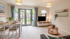 A modern living room with a dining area, large windows, and a flat-screen TV. - 2 Bed in Mundesley (oc-r31875) (Mundesley)