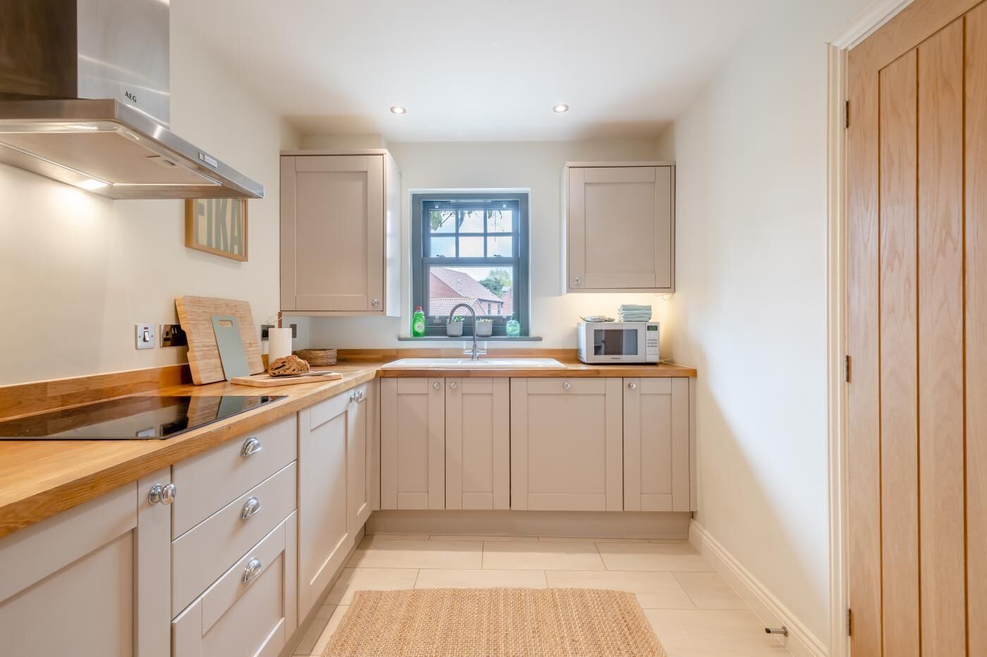 A compact kitchen with wooden cabinets, a stainless steel range hood, a microwave, and a window providing natural light.