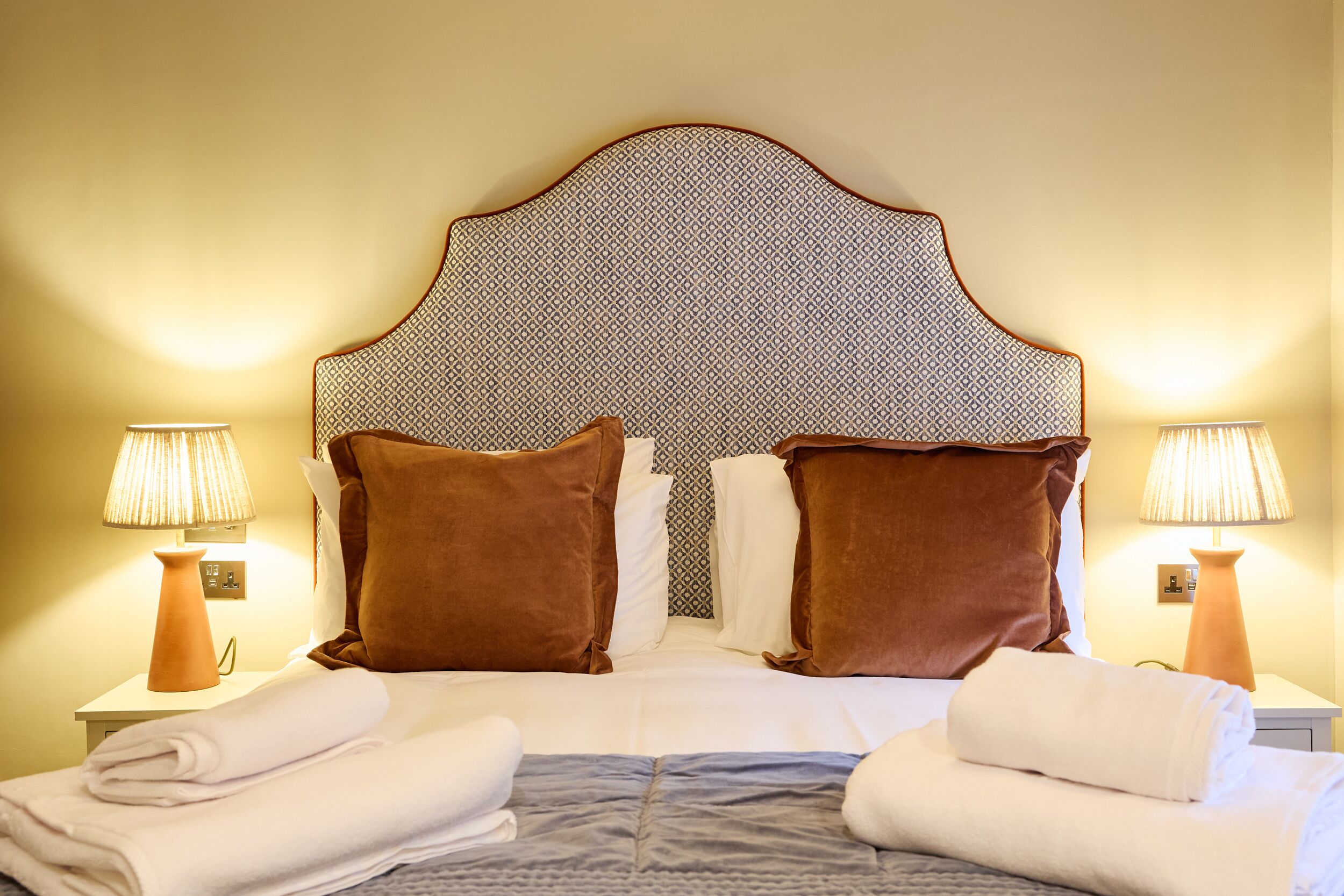 A neatly made bed with a patterned headboard, two brown pillows, and two white towels.