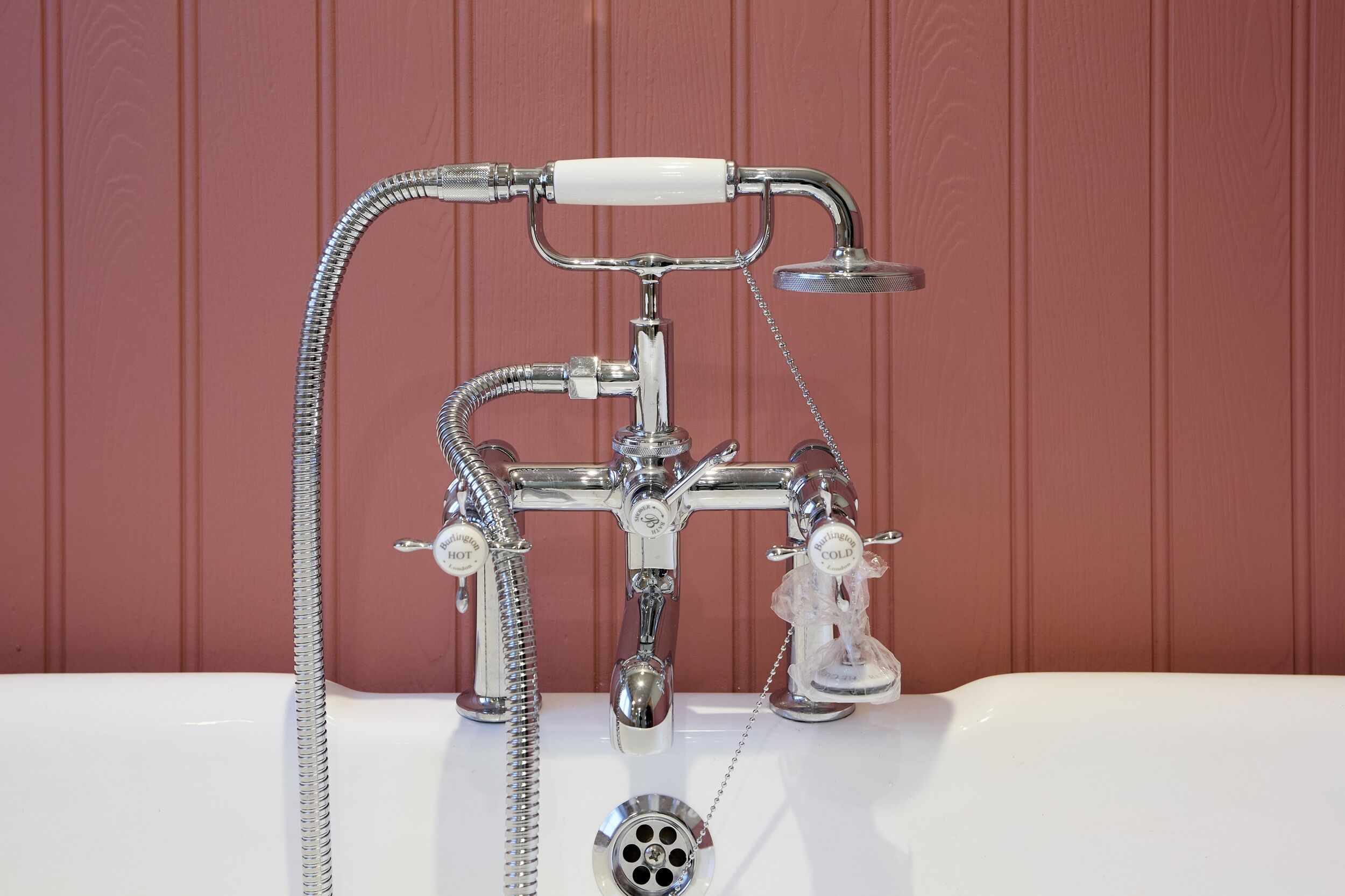 Un baño de estilo vintage con una bañera blanca, un cabezal de ducha cromado y un grifo de ducha aparte.