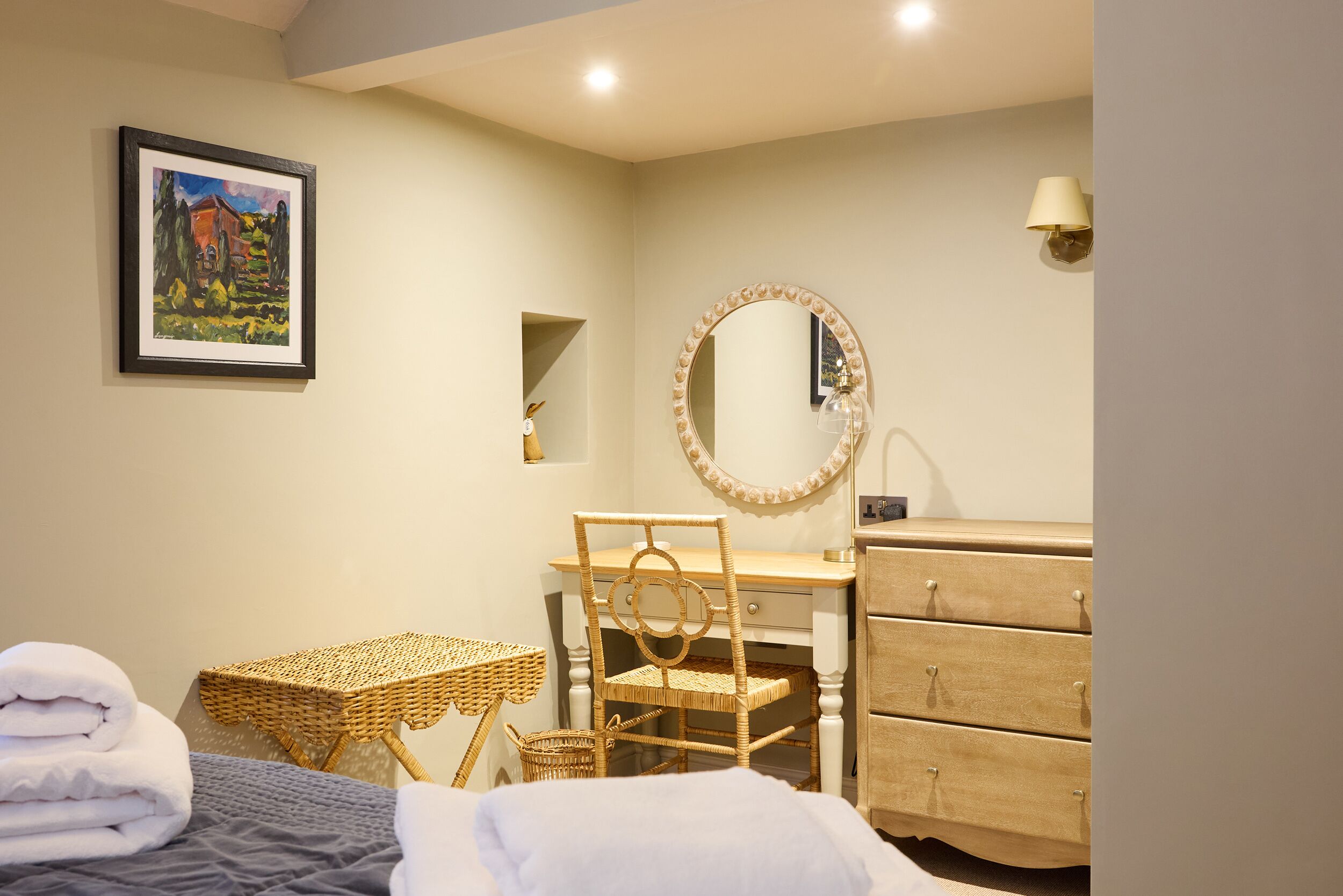 A neatly arranged bedroom with a bed, a desk, a chair, a dresser, and a framed painting on the wall.