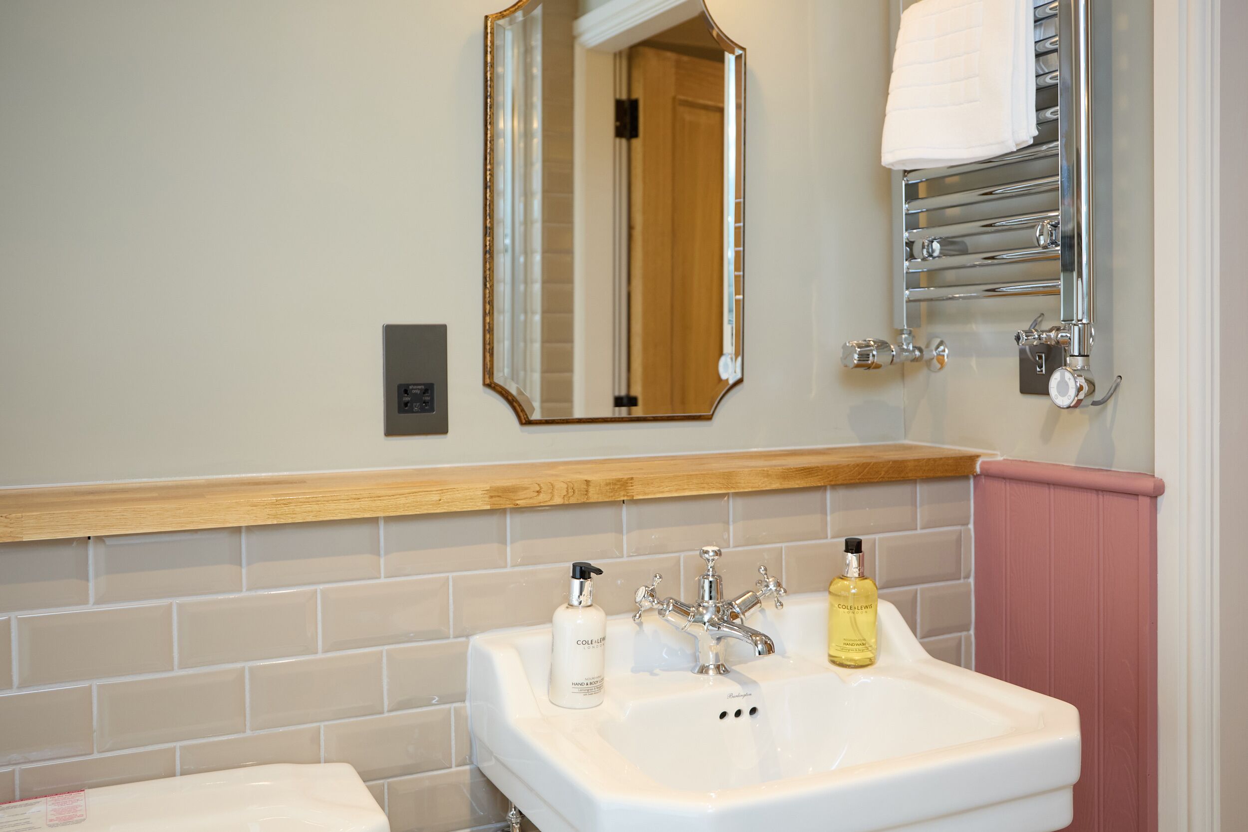 A bathroom with a white sink, a mirror, a towel rack, and a bottle of hand soap.