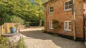 Une maison à deux étages, construite en briques, avec une allée en gravier et une clôture en bois.