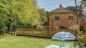 Une maison en briques avec un jardin clôturé, une clôture en bois, une table, des chaises et un parasol.