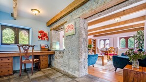 Eine rustikale Küche mit Steinwänden, Holzbalken und einem Essbereich mit blauem Stuhl und Holztisch.