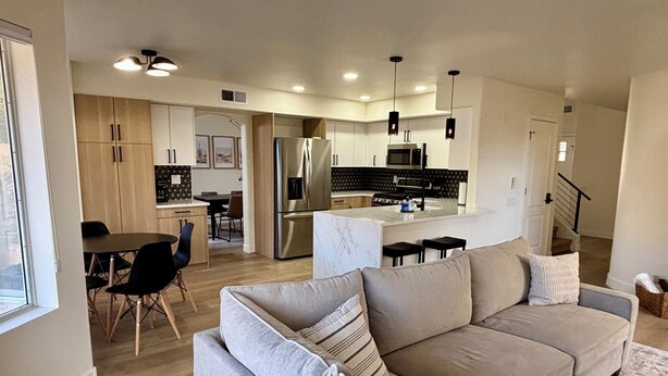 A modern living room with a grey sofa, a dining area with a table and chairs, and a kitchen with a refrigerator and microwave. - Walk to Sabino Canyon Trails, 4Bd Home with Hot Tub (Tucson)