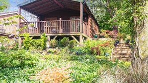 A wooden cabin with a balcony, surrounded by a garden with various plants and flowers. - 1 Bed in Milton Abbas (oc-w32019) (Milton Abbas)