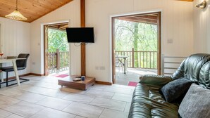 A cozy cabin interior with a wooden ceiling, a flat-screen TV mounted on the wall, a leather sofa, and a dining area with a table and chairs. - 1 Bed in Milton Abbas (oc-w32019) (Milton Abbas)