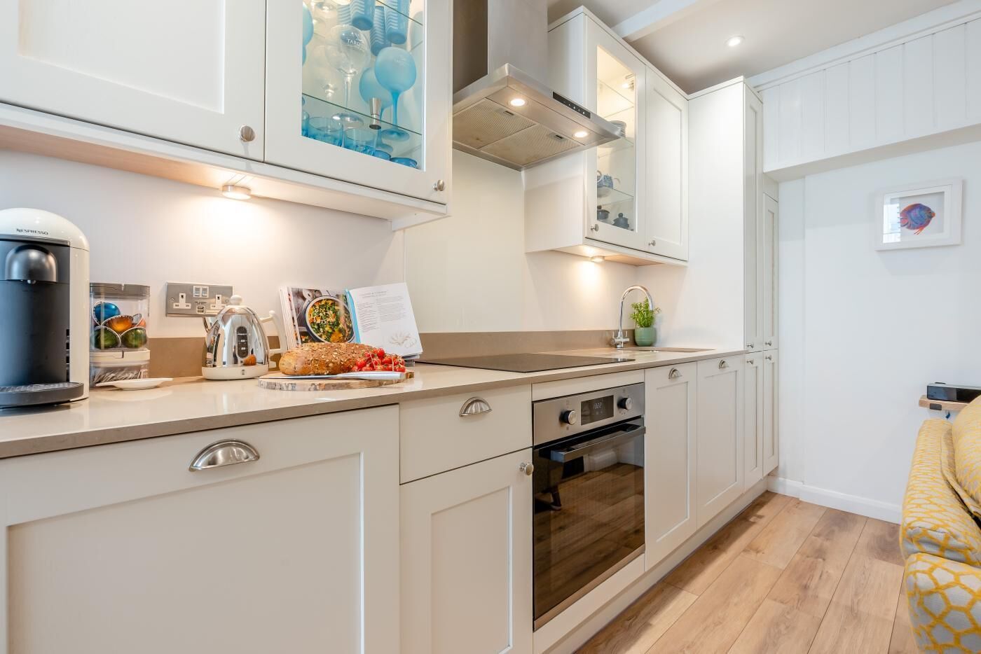 A modern kitchen with white cabinetry, a built-in oven, and a coffee machine.