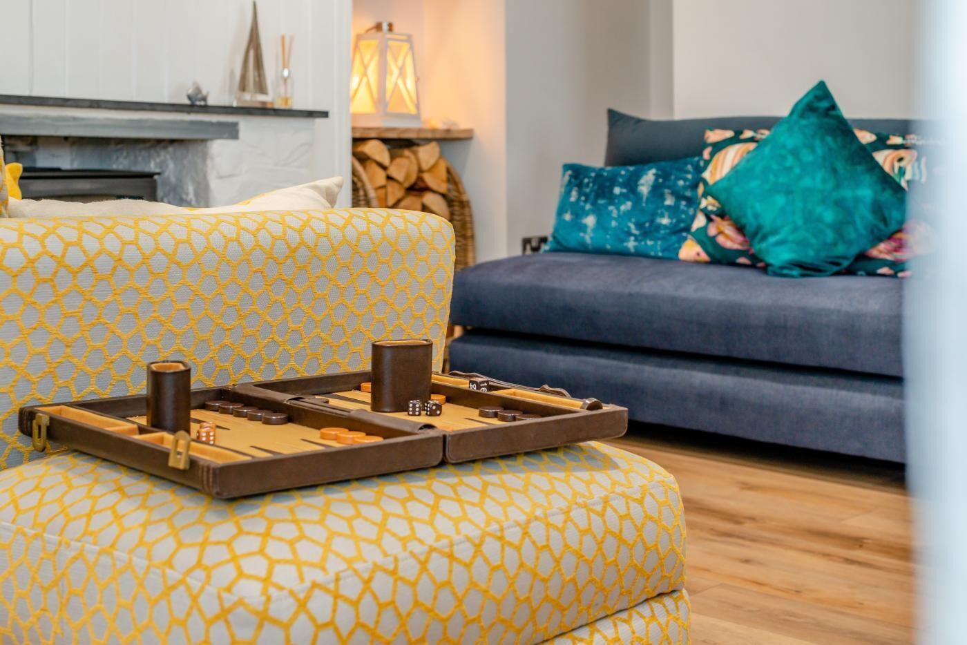 A living room with a patterned yellow armchair, a blue sofa with decorative pillows, and a board game on the armchair.