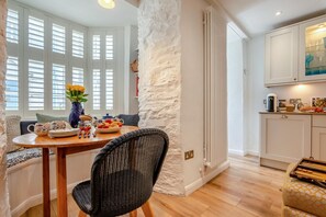 Un coin repas avec une table ronde en bois, une chaise noire en osier et un vase rempli de fleurs jaunes.