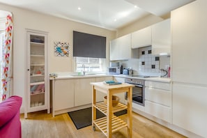 A modern kitchen with white cabinetry, a built-in oven, and a microwave. There is a small wooden table with a bowl and a book.