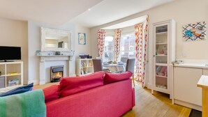 A living room with a red sofa, a fireplace, a television, and a dining area with a table and chairs. - 1 Bed in Southwold (oc-bate) (Southwold)