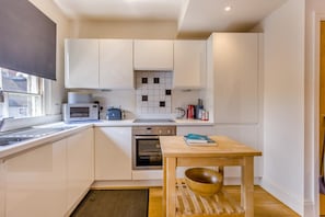 Eine kleine Küche mit weißen Schränken, einer Mikrowelle, einem Toaster und einem Holztisch mit einer Schüssel.