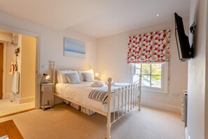 A bedroom with a bed, bedside tables, a window with a patterned valance, and a television mounted on the wall. - 1 Bed in Southwold (oc-bate) (Southwold)