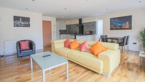 A modern living room with a sofa, a coffee table, a dining table with chairs, and a kitchen in the background. - Stylish modern newly built apartment (Edinburgh)