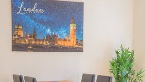A dining area with a table and chairs, a painting of London landmarks, a green plant, and a yellow sofa with orange cushions. - Stylish modern newly built apartment (Edinburgh)